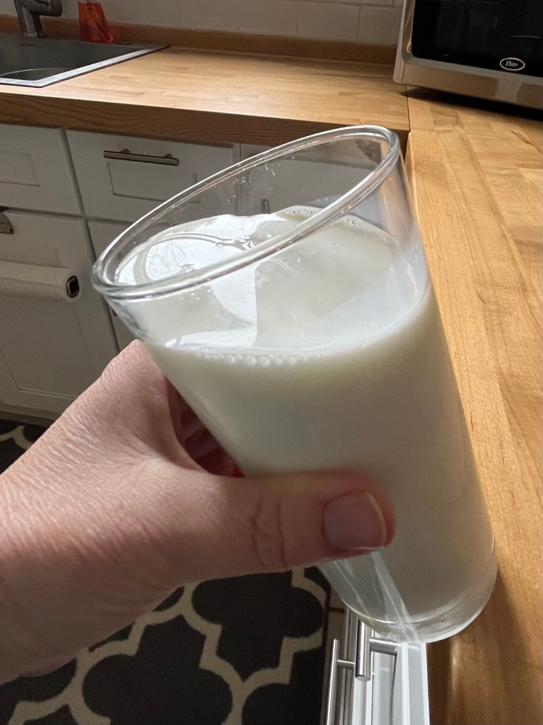 picture of a full glass of milk being grabbed by a hand as it teeters on the edge of a kitchen counter